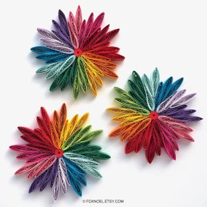 Könnte beinhalten: Drei kreisförmige Papier-Quilling-Kunstwerke in einer Gruppe angeordnet. Jedes Stück zeigt einen lebendigen Regenbogen-Farbverlauf aus eng gewickelten Papierstreifen, die als längliche Blütenblätter von einer roten Mitte ausgehen. Text FOXNOEL.ETSY.COM.