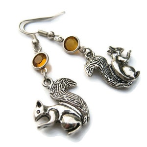 May include: A pair of silver dangle earrings featuring a squirrel charm and amber-colored glass beads.