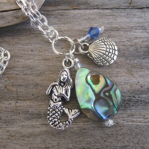May include: A silver chain necklace with a mermaid charm, a seashell charm, and a green abalone shell pendant.