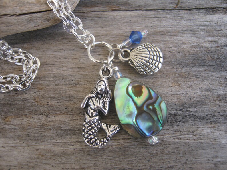 May include: A silver chain necklace with a mermaid charm, a seashell charm, and a green abalone shell pendant.
