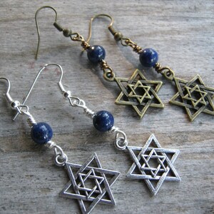 Pu&ograve; includere: Un paio di orecchini con una pietra preziosa blu e un ciondolo a forma di Stella di David in argento. Gli orecchini sono su una superficie di legno.