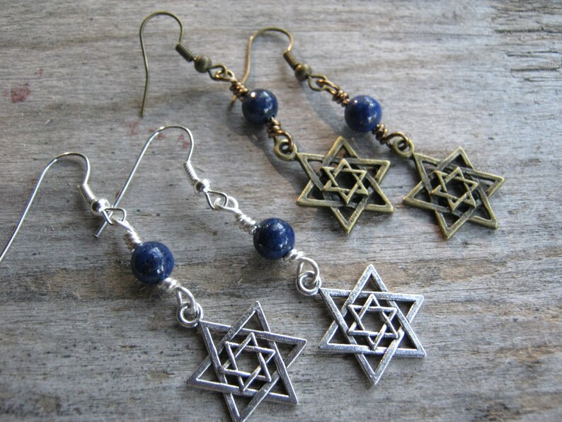 Pu&ograve; includere: Un paio di orecchini con una pietra preziosa blu e un ciondolo a forma di Stella di David in argento. Gli orecchini sono su una superficie di legno.