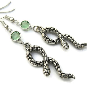May include: A pair of silver snake earrings with green gemstone accents. The snake is coiled and has a textured surface.