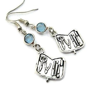 May include: Silver earrings with a blue crystal charm and a charm shaped like an open pocket knife with tools inside.