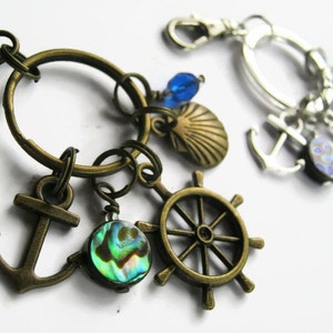May include: A bronze key chain with nautical charms, including an anchor, a ship's wheel, a seashell, and a blue iridescent abalone shell.