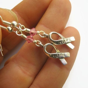 May include: Silver earrings with pink crystal beads and silver ribbon charms that say "HOPE".
