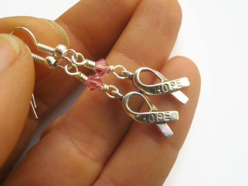 May include: Silver earrings with pink crystal beads and silver ribbon charms that say "HOPE".