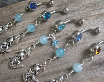 May include: Five silver mermaid charm belly button rings with blue and turquoise beads. Each ring has a different colored gem stone.