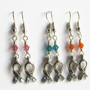 May include: Three pairs of silver earrings with a silver ribbon charm that says "HOPE". Each pair has a different colored crystal bead: pink, teal, and orange.
