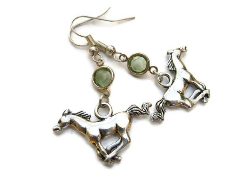 May include: Silver tone earrings with green glass stones and a horse charm. The horse is running.