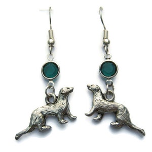 May include: Silver dangle earrings featuring a silver ferret charm and a dark green crystal.