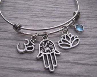 May include: A silver charm bracelet with multiple charms, including a hamsa hand, an om symbol, a lotus flower, and a light blue crystal charm.