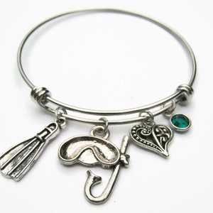 May include: Silver charm bracelet with a green gem, a heart, a diving mask, and a pair of flippers.
