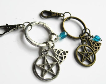 May include: Two silver keychains with charms. One keychain has a silver pentagram charm, a silver Celtic knot charm, and blue glass beads. The other keychain has a bronze pentagram charm, a bronze Celtic knot charm, and blue glass beads.