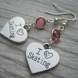 May include: A pair of silver heart-shaped earrings with pink crystal accents. The earrings feature the text "I ♥ Skating" on each heart.