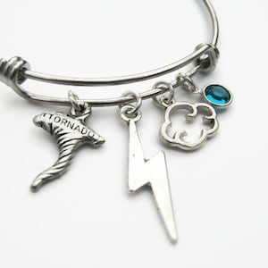 May include: A silver charm bracelet with a tornado, lightning bolt, cloud, and a blue gemstone charm. The bracelet is expandable and has a silver clasp.