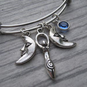 May include: A silver charm bracelet with three charms: a crescent moon, a goddess figure, and a blue crystal. The bracelet is made of stainless steel and has a spring clasp.