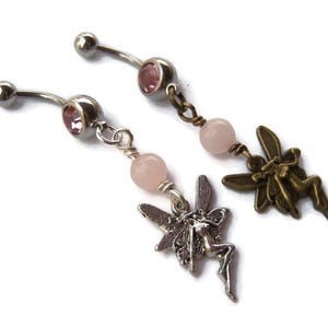 May include: Two belly button rings with a fairy theme. One ring has a silver finish with a fairy charm and pink gemstone accents. The other ring has a bronze finish with a fairy charm and pink gemstone accents.