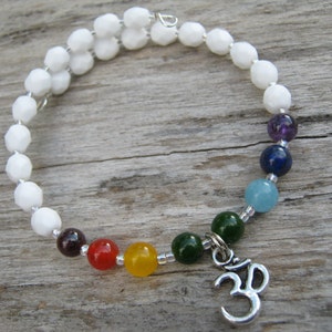 May include: White beaded bracelet with a charm of the Om symbol and seven chakra stones in the colors of the rainbow.