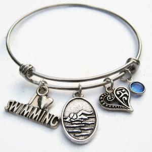 May include: A silver expandable bangle bracelet with four charms. The charms include a swimmer, a heart with a swirl design, a heart with the words "I love swimming", and a blue crystal.