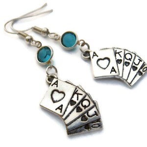 May include: A pair of silver earrings with a teal blue crystal and a charm of playing cards, including the Ace of Hearts and the King, Queen, Jack, and Ten of Hearts.