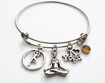 May include: A silver charm bracelet with four charms: a yoga pose, a yoga symbol, a heart with the text "I love yoga", and a small amber-colored gemstone.
