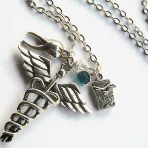 Puede incluir: Collar de plata con un dije de caduceo médico, un dije de diente, una gema azul turquesa y un dije que dice "FLOSS".