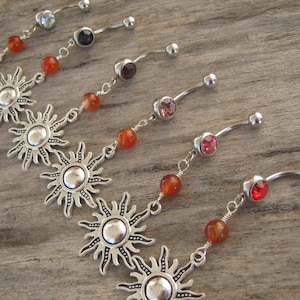 May include: A set of six belly button rings with silver sun charms and red, pink, and clear crystals.
