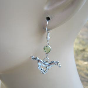 May include: Silver dangle earrings with a green gemstone and a silver horse charm.