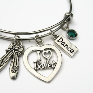 May include: Silver charm bracelet with a heart charm that says "I love Ballet", a pair of ballet shoe charms, a charm that says "Dance", and a green gem charm.
