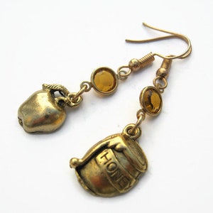 May include: Gold tone earrings with a honey pot charm and an apple charm. Each earring has two amber coloured glass beads.
