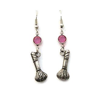 May include: A pair of silver earrings with pink crystal accents and a silver makeup brush charm.