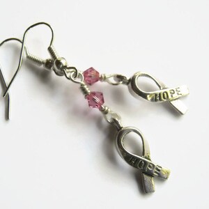 May include: Silver earrings with pink crystal beads and a silver ribbon charm with the word "HOPE" on it.