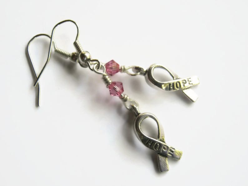 May include: Silver earrings with pink crystal beads and a silver ribbon charm with the word "HOPE" on it.