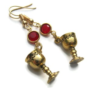 May include: Gold tone earrings with red gemstone accents and a dangling chalice charm.