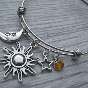 May include: A silver charm bracelet with a sun, moon, star, and amber-colored crystal charm.