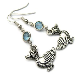 May include: Silver dangle earrings with a duck charm and light blue crystal accents.