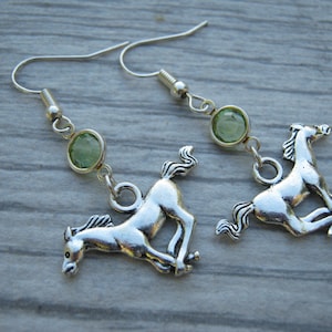 May include: Silver horse earrings with green gemstone accents. The horses are in a running pose.