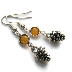 May include: A pair of silver dangle earrings with amber-colored crystal stones and silver pine cone charms.
