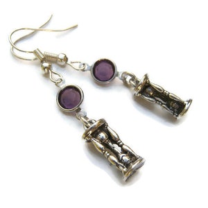 May include: A pair of silver earrings with purple glass stones and a silver hourglass charm.