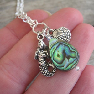 May include: Silver chain necklace with a mermaid charm, a seashell charm, and a green abalone shell pendant.