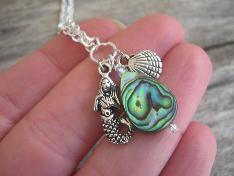 May include: Silver chain necklace with a mermaid charm, a seashell charm, and a green abalone shell pendant.