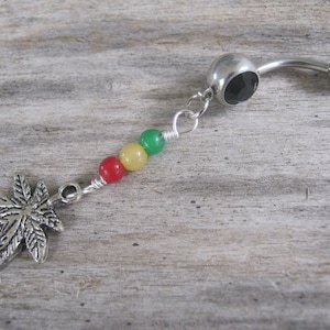 Puede incluir: Un piercing de ombligo plateado con una gema negra, un dije de hoja de marihuana plateado y cuentas rojas, amarillas y verdes.