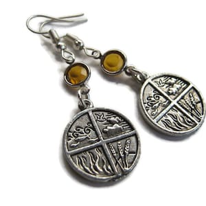 May include: Silver earrings with a round charm featuring four elements: air, earth, fire, and water. Each element is depicted in a stylized design. The earrings have amber-colored crystal accents.