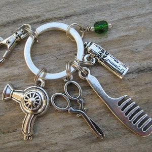 Puede incluir: Llavero de plata con un secador de pelo, un peine, unas tijeras y un frasco de laca para el cabello con encanto. Los encantos están unidos a un anillo de plata con un cierre de plata.