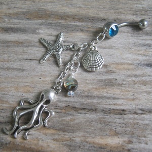 May include: Silver belly button ring with a blue gem, a starfish, a seashell, an abalone shell, and an octopus charm.