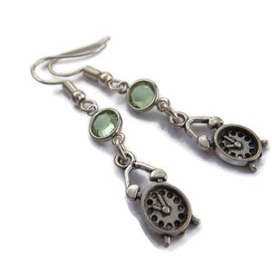 Puede incluir: Pendientes de plata con detalles de cristal verde y un dije de reloj.