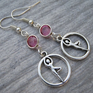 May include: Silver earrings with pink crystal accents and a silver charm of a person in a yoga pose.