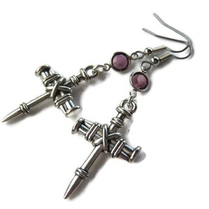 May include: Silver cross earrings with purple crystal accents. The crosses are detailed with a woven design and have a pointed tip.