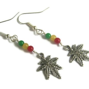 Puede incluir: Pendientes de plata con cuentas verdes, amarillas y rojas y un dije de hoja de marihuana de plata.